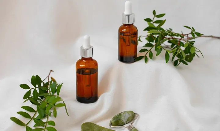 Two brown dropper bottles surrounded by green leaves on a white background.
